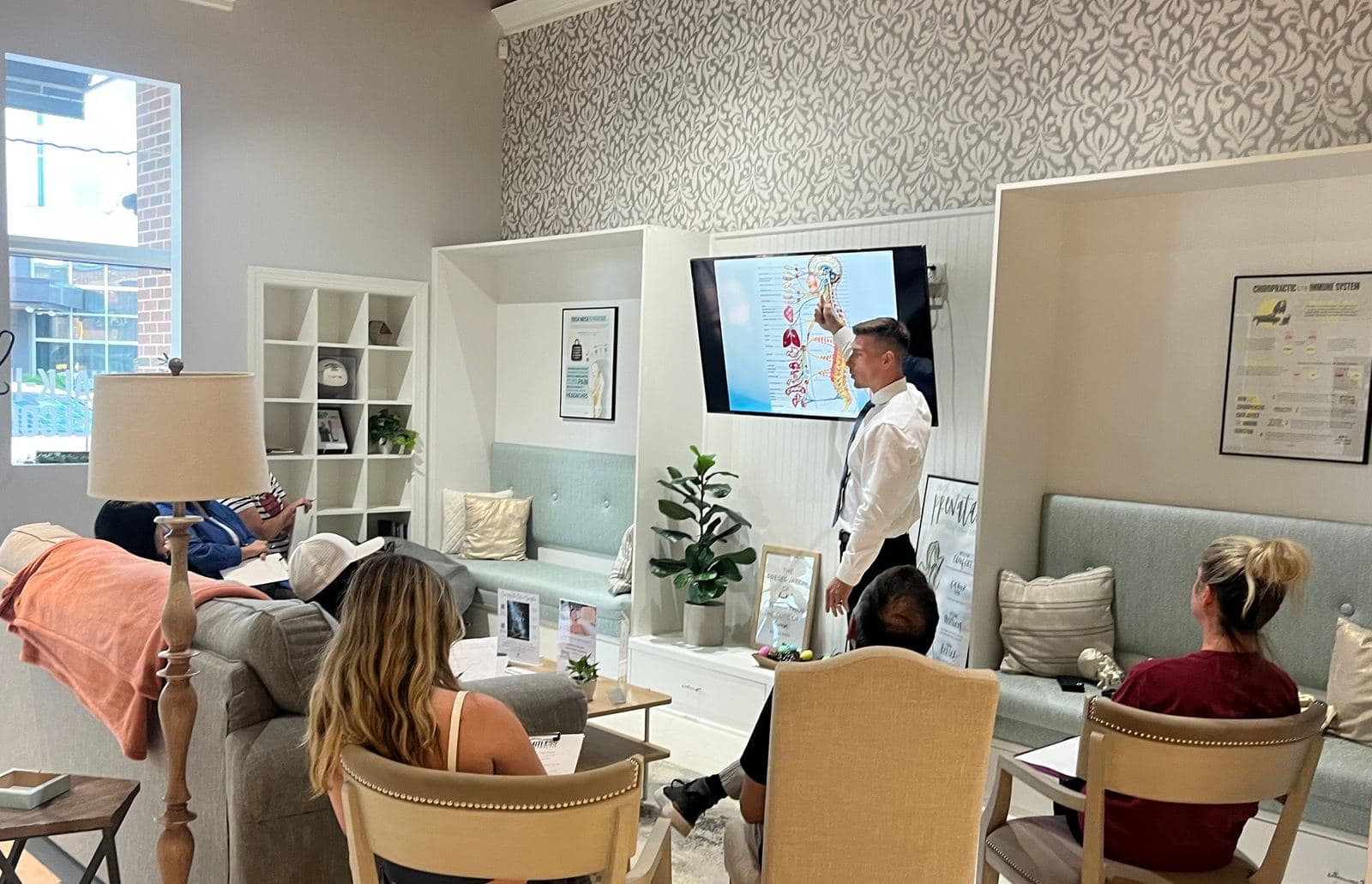 Dr. Tim Hartman pointing at a spine and nervous system slide while guests watch from chairs and couches in the Limitless Chiropractic front room